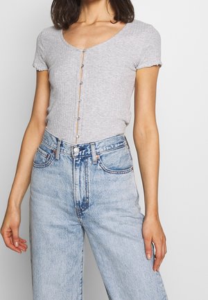 Grijs geribbeld topje met korte mouwen met een diepe V-hals en knoopsluiting, gecombineerd met lichtblauwe high-waisted wijde jeans.