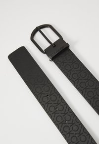 Cintura sintetica nera con un motivo testurizzato e fibbia in metallo nero rettangolare con il logo del marchio. Finitura liscia, fori regolabili.