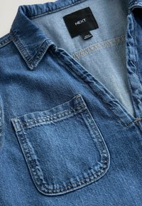Medium sininen denim-paita, jossa on napitön V-pääntie, terävä kaulus ja yksi rintatasku siisteillä ompelutiedoilla.