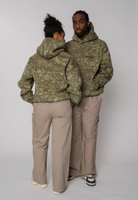 Sweat-shirts à capuche verts à motif camouflage, coupe décontractée avec poches avant, assortis à des pantalons cargo beige clair avec poches latérales et jambes amples.