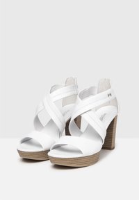 White high-heeled sandals with crisscross straps, open toe, wooden-textured block heel, and smooth leather finish.