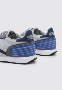 Zapatillas de hombre en gris claro con detalles en azul marino y azul. Cuentan con una suela texturizada y un contrafuerte con estrías que presenta el logotipo.
