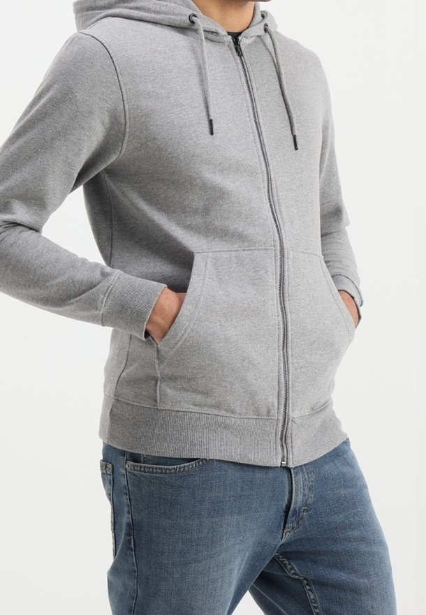 Grå zip-up hættejakke med kangaroo-lomme, snoretræk i hætten, ribbede manchetter og kant; lavet af blødt stof, båret med blå jeans.