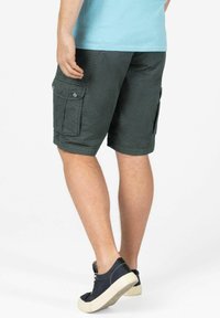 Grüne Cargo-Shorts aus strukturiertem Stoff verfügen über zwei seitliche Taschen mit Klappen, haben einen lockeren Schnitt und sind mit dunklen Sneakers kombiniert.