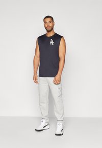 Camiseta sin mangas de color navy con logo blanco "LA", combinada con pantalones de chándal cargo gris claro que tienen bolsillos, y zapatillas deportivas en blanco y negro.