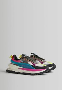 Barevné tenisky s robustní, vrstvenou podrážkou, vyrobené z síťoviny a kůže, s černými tkaničkami a neonovými akcenty.