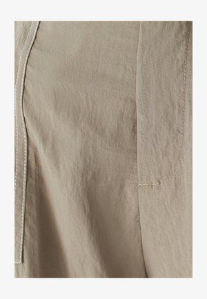Light beige fabric featuring a smooth texture with subtle wrinkles. Visible stitching in a contrasting color along seams.