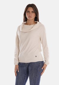 Maglione a collo alto in maglia beige chiaro, materiale morbido, maniche lunghe, orlo a costine, con un piccolo logo laterale.