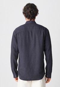 Marineblaue Langarmbluse mit button-down Kragen, strukturiertem Stoff und detaillierten Nähten an den Manschetten und am Rücken.