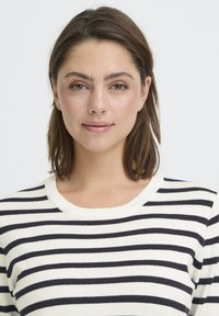 Pull rayé avec des lignes horizontales bleu marine et crème, col rond, texture douce et coupe légèrement décontractée.