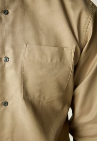 Béžová, texturovaná košile na knoflíky s malou náprsní kapsou a šedými knoflíky. Má mřížkovaný vzor a límečkový výstřih.