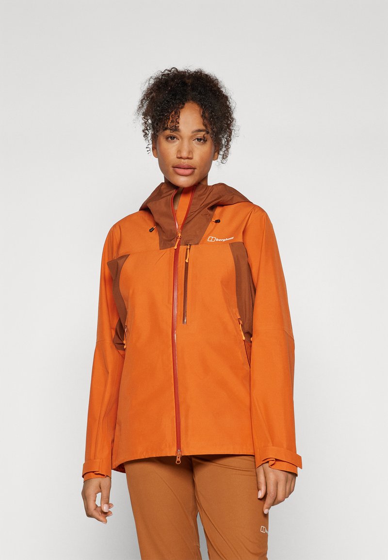 Orange waterproof jacket with brown accents, zipper pockets, adjustable cuffs, and a hood. Smooth texture, designed for outdoor activity.