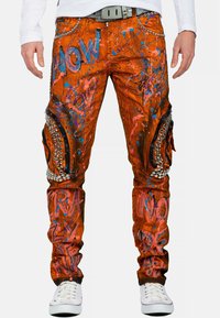 Oranje denim broek met opvallende blauwe en roze spetters, metalen studs en kniezakken met zwarte stoffen accenten.