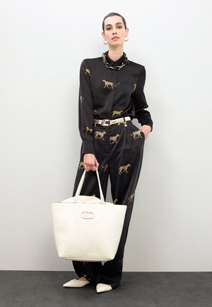 Conjunto de satén negro con estampado de leopardo dorado, con cinturón. Bolso tote color crema con logo en relieve. Zapatos planos blancos puntiagudos completan el look.