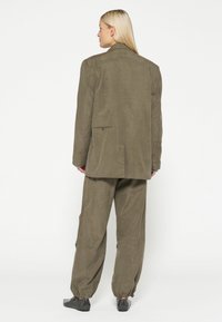 Completo a due pezzi verde oliva con giacca dal taglio morbido e pantaloni con polsini elasticizzati, caratterizzato da un tessuto testurizzato e dettagli delle tasche discreti.