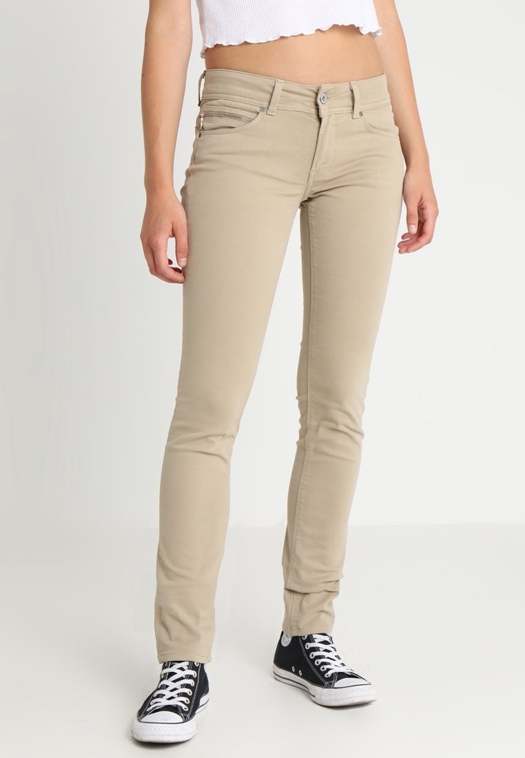 Bežové skinny džíny s středním pasem, obsahující přední a zadní kapsy, a úzký střih, doplněné černobílými teniskami.