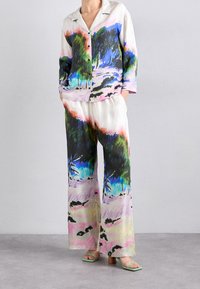 Avslappnad passform, flerfärgad linneset med abstrakt naturtryck, som inkluderar en skjorta med knäppning och byxor med vida ben. Gröna sandaler kompletterar looken.