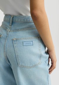 Jeans din denim de un albastru deschis, cu talie înaltă, având un buzunar posterior cu eticheta albastră LIU JO și cusături contrastante galbene.