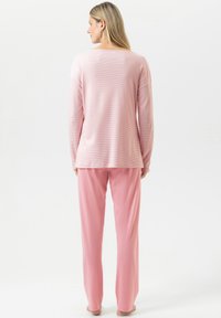 Haut à manches longues rose pâle avec de fines rayures horizontales, associé à un pantalon ample assorti, tous deux en tissu doux.