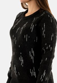 Suéter de lana negra con un patrón texturizado de rayas verticales blancas. El diseño se completa con un escote redondo y puños acanalados.