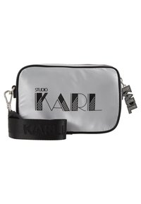 Silberne Nylon-Crossbody-Tasche mit schwarzem Branding. Sie hat eine rechteckige Form, einen Reißverschluss und einen verstellbaren Gurt mit geprägt Text.