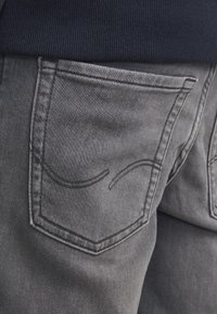 Nærbilde av grå denim jeanslomme med dekorative sømmer og en marineblå ribbet toppkant over.