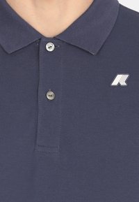 Polo shirt blu navy realizzato in tessuto testurizzato con colletto. Presenta due bottoni argento e un piccolo logo bianco sul lato sinistro del petto.