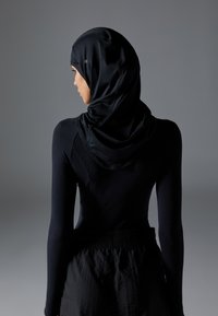 Svart atletisk langermet topp med en matchende svart strukturert hijab. Glatt, elastisk stoff med en tettsittende silhuett og rynkede detaljer ved halsen.