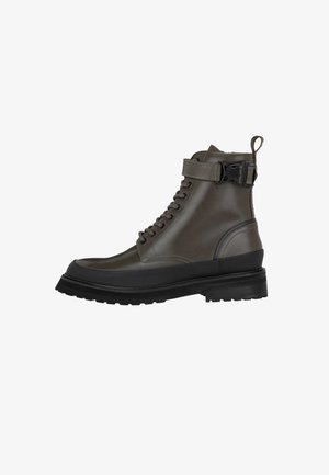 Dunkelgrüner Lederknöchelstiefel mit runder Zehe, Schnürung vorne, verstellbarem seitlichem Riemen und dicker schwarzer Sohle mit strukturiertem Profil.