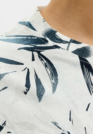 Zbliżenie na białą tkaninę z dużym czarnym abstrakcyjnym wzorem liści oraz widocznym przeszyciem wzdłuż zakrzywionego szwu.