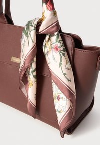 Sac à main synthétique marron avec un dessus incurvé, orné d'un foulard en soie à motifs floraux noué autour de la poignée. Du matériel doré affiche le nom de la marque.