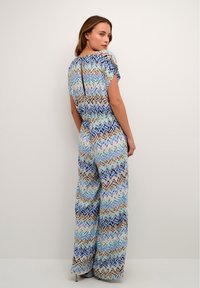 Värvikas mustriga kombinesoon, millel on lühikesed varrukad ja võtmeaugu seljas, valmistatud kergest kangast sinise ja beeži tooni.