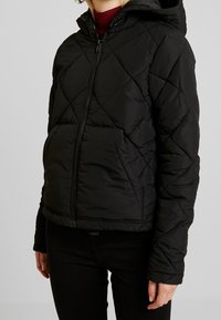 Black quilted puffer jacket with a zip front, hood, and elastic cuffs. Features diamond-shaped stitching and front pockets.