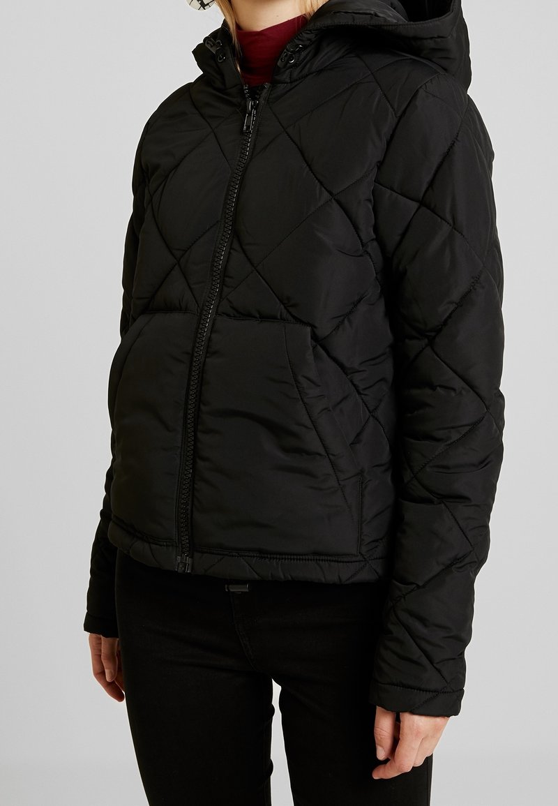 Black quilted puffer jacket with a zip front, hood, and elastic cuffs. Features diamond-shaped stitching and front pockets.