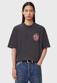 Czarny, oversize t-shirt wykonany z bawełny, z różowym okrągłym logo na lewej piersi, okrągłym dekoltem i krótkimi rękawami.