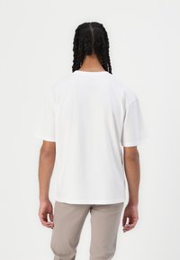 White short-sleeve t-shirt with a relaxed fit, made of smooth cotton fabric, featuring a round neckline and straight hem, shown from the back.