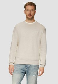 Hellbeige Pullover mit rundem Ausschnitt, gerippten Bündchen und Saum sowie einem strukturierten Strickmuster, kombiniert mit ausgewaschenen blauen Jeans.