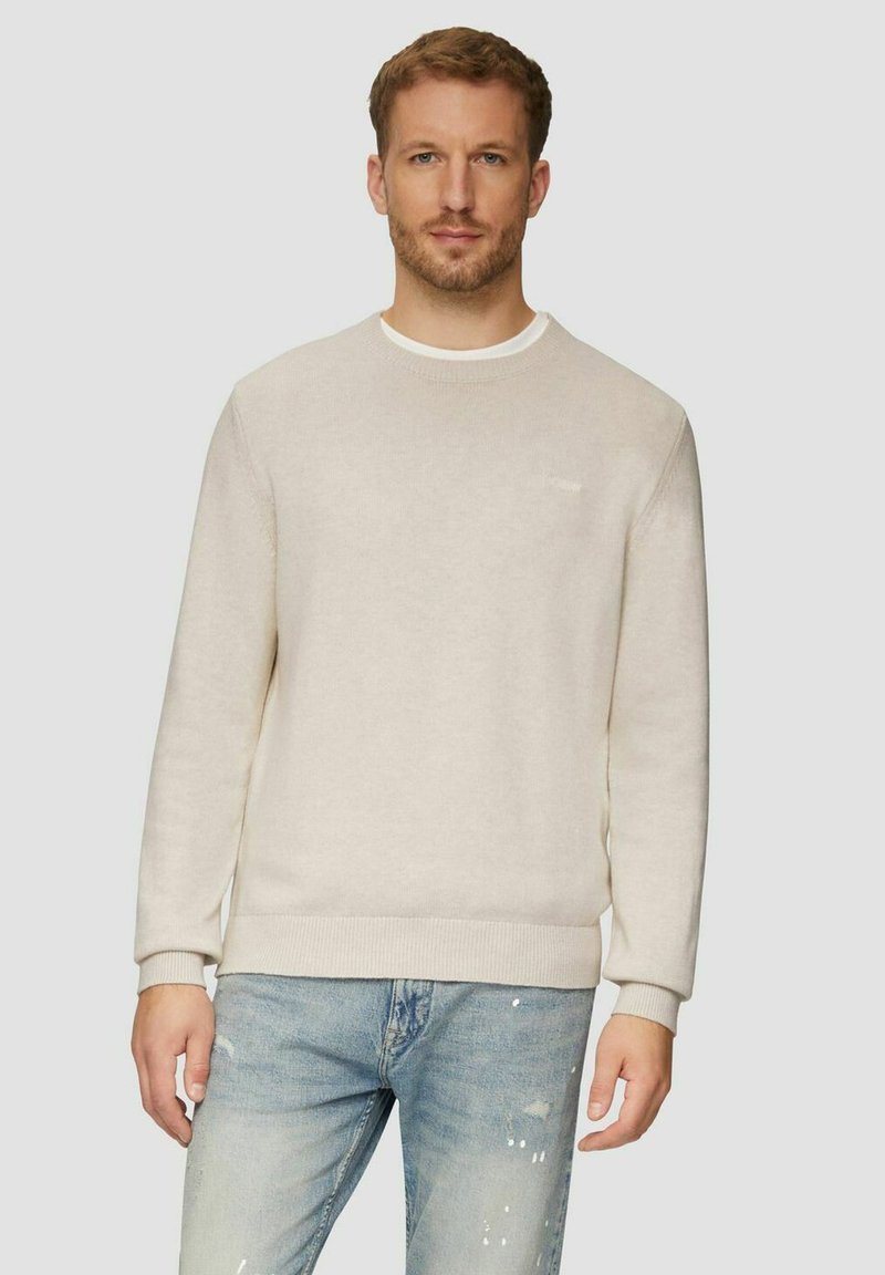 Hellbeige Pullover mit rundem Ausschnitt, gerippten Bündchen und Saum sowie einem strukturierten Strickmuster, kombiniert mit ausgewaschenen blauen Jeans.