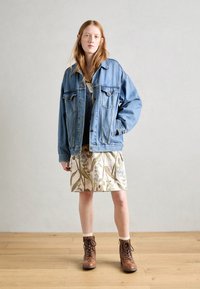 Veste en denim avec deux poches poitrine, une coupe décontractée, sur une robe à imprimé floral arrivant au genou. Des bottines lacées marron finalisent le look.