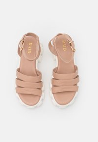 Beige strappy sandals with three bands on the upper, a chunky white sole, and a side buckle accent for adjustable fit. Brand labeled inside.