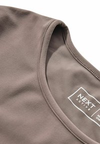 Haut de sport en tissu marron doux ; présente un col arrondi, une texture douce et un subtil détail de couture près du col. Étiquette de la marque visible.