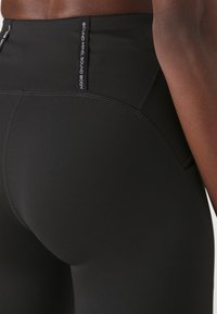 Black athletic leggings with a high waistband, featuring a smooth texture, seam detailing, and a side tag reading "SOUND MIND SOUND BODY."
