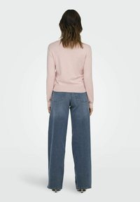 Un pull en maille rose clair avec une taille cintrée, associé à un jean en denim bleu à jambes larges. La tenue offre une coupe décontractée et confortable.
