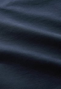 Sötét tengerészkék anyag sima textúrával, lágy hullámokkal és redőkkel, finom fényt és egyenletes felületet mutat. 