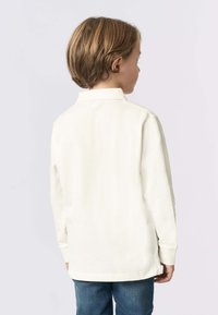 Polo a maniche lunghe di colore crema chiaro, in materiale cotone con colletto, presenta un orlo dritto e una vestibilità standard, indossato da un bambino visto da dietro.