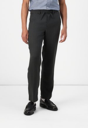 Mørkegrå, smale bukser med en glat tekstur, elastisk talje og snor. Båret med sorte loafers.