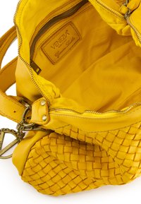 Gelbe Lederhandtasche mit gewebter Textur, Reißverschluss und einem gebrandeten Lederanhänger im Inneren. Das Innenfutter ist ebenfalls gelb.