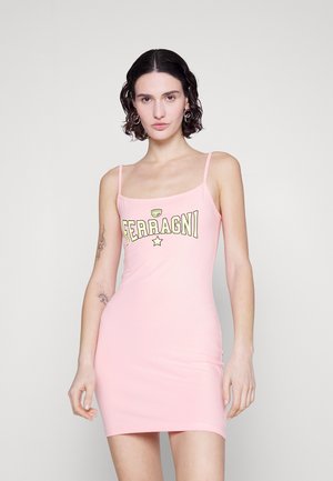 Γυναίκα με κοντά σγουρά μαλλιά, φορώντας ένα ροζ αμάνικο μίνι φορεματάκι με την ένδειξη "FERRAGNI" και τατουάζ στα χέρια της, που στέκεται μπροστά σε λευκό φόντο.