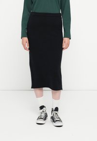 Jupe crayon en maille noire au design ajusté, longueur genou, avec une texture lisse et une taille élastique, associée à des baskets montantes.