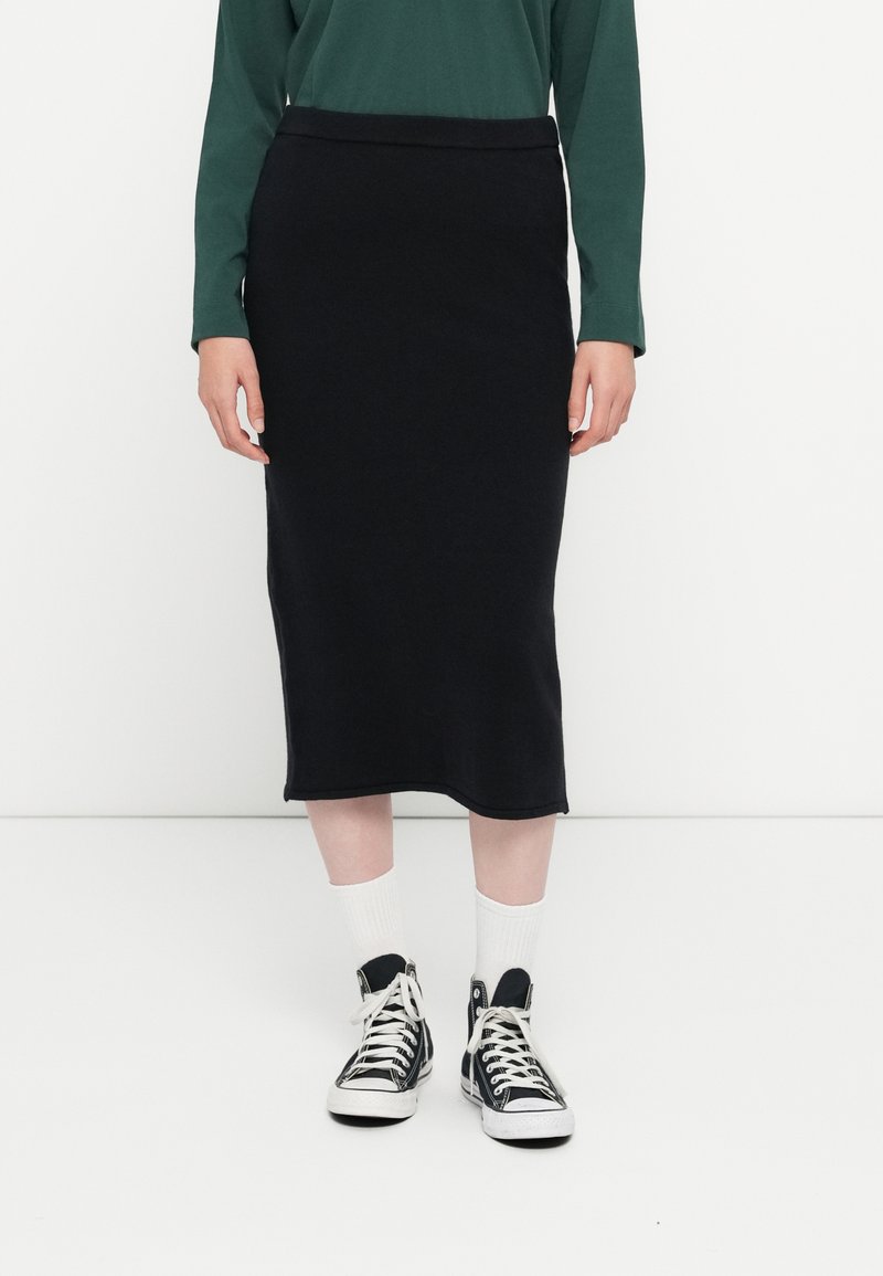 Jupe crayon en maille noire au design ajusté, longueur genou, avec une texture lisse et une taille élastique, associée à des baskets montantes.